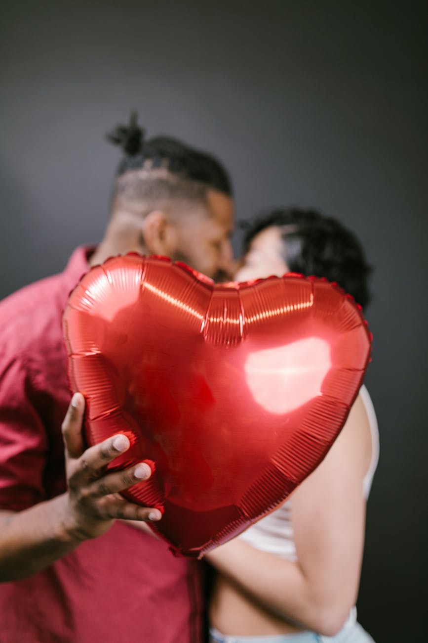 couple kissing while holding a red heart shaped balloon