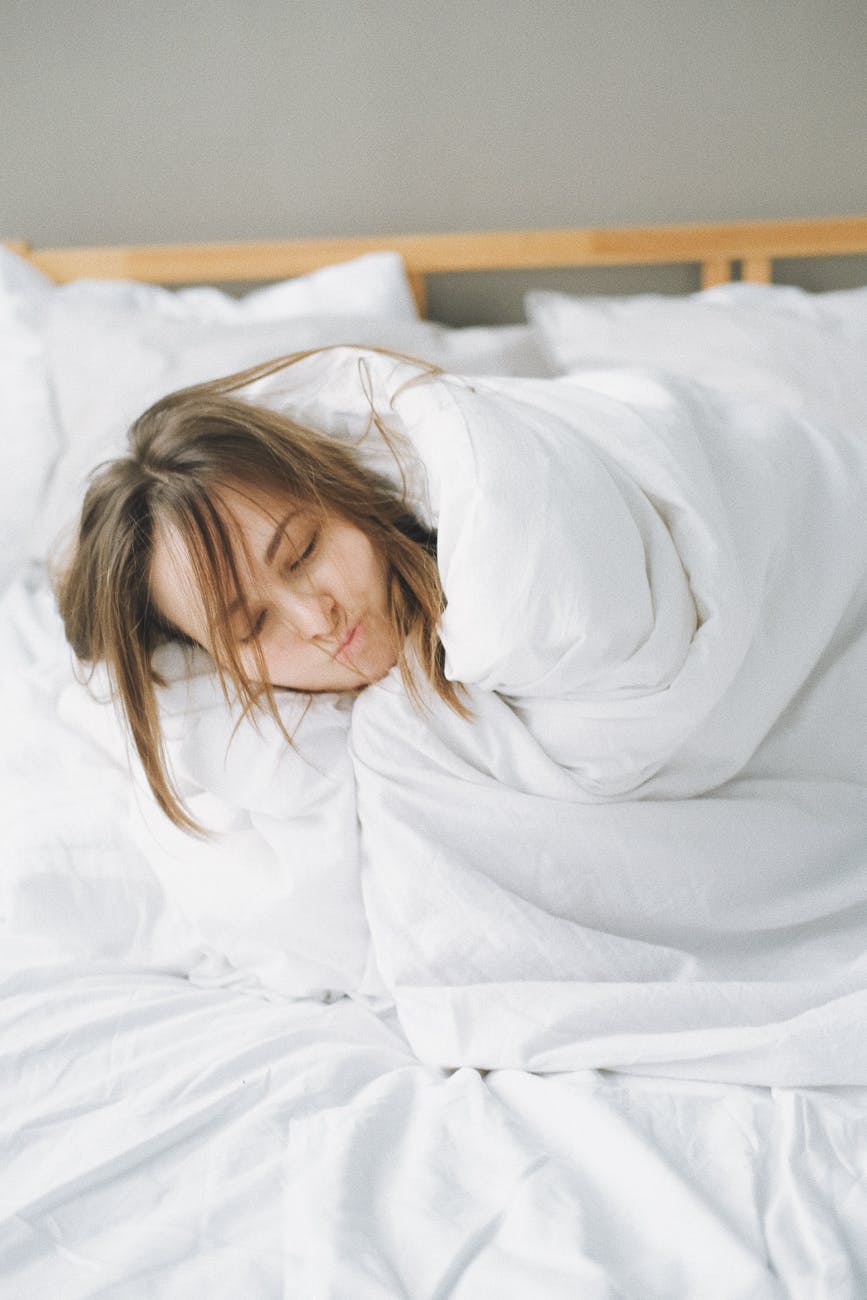 woman covered in white blanket lying on bed