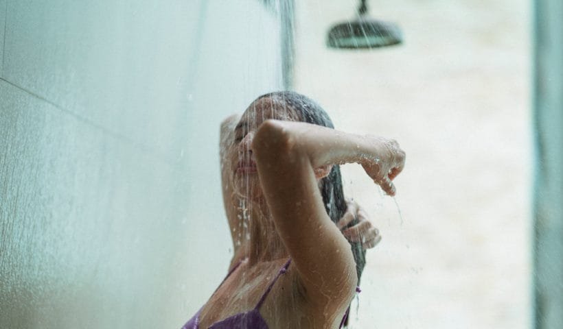 young female in swimsuit rinsing hair in shower