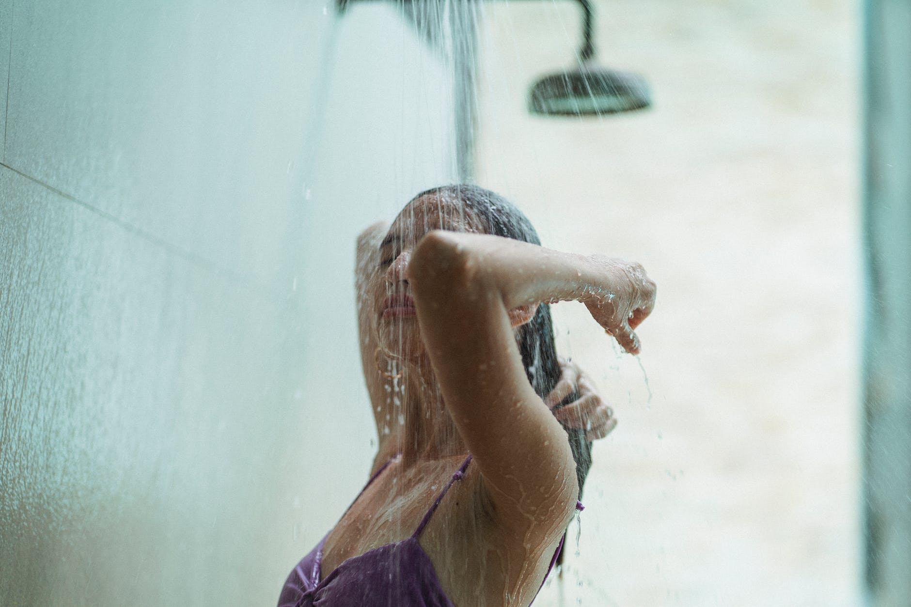 young female in swimsuit rinsing hair in shower