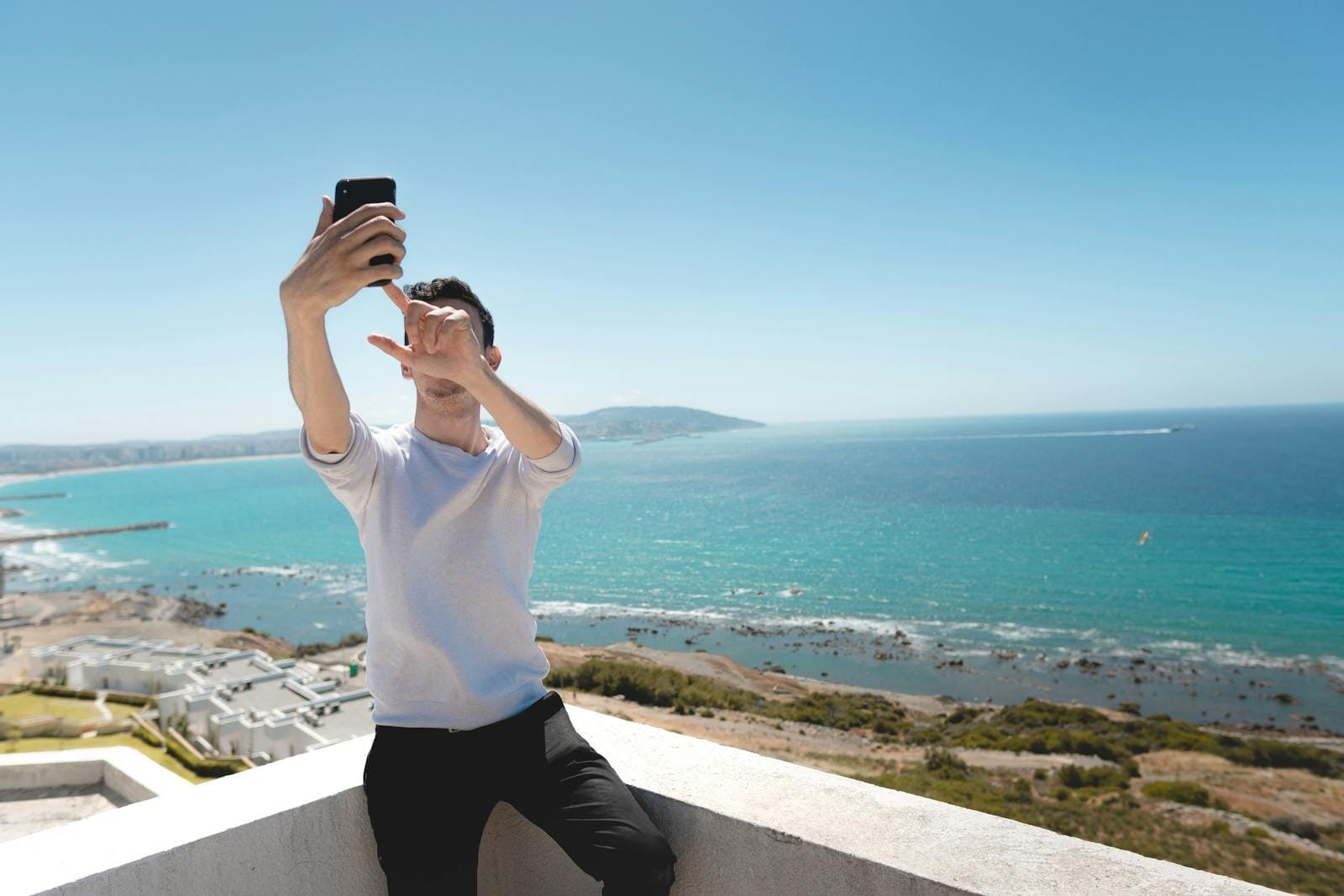Man capturing a selfie with a stunning ocean backdrop, symbolizing travel and leisure.