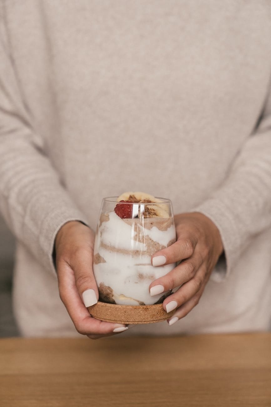 person in beige long sleeves holding a clear glass of yoghurt