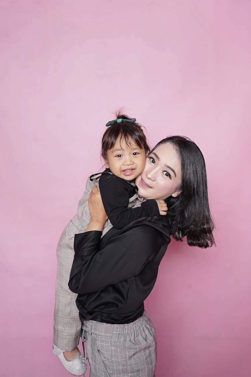 woman holding toddler girl against pink wall
