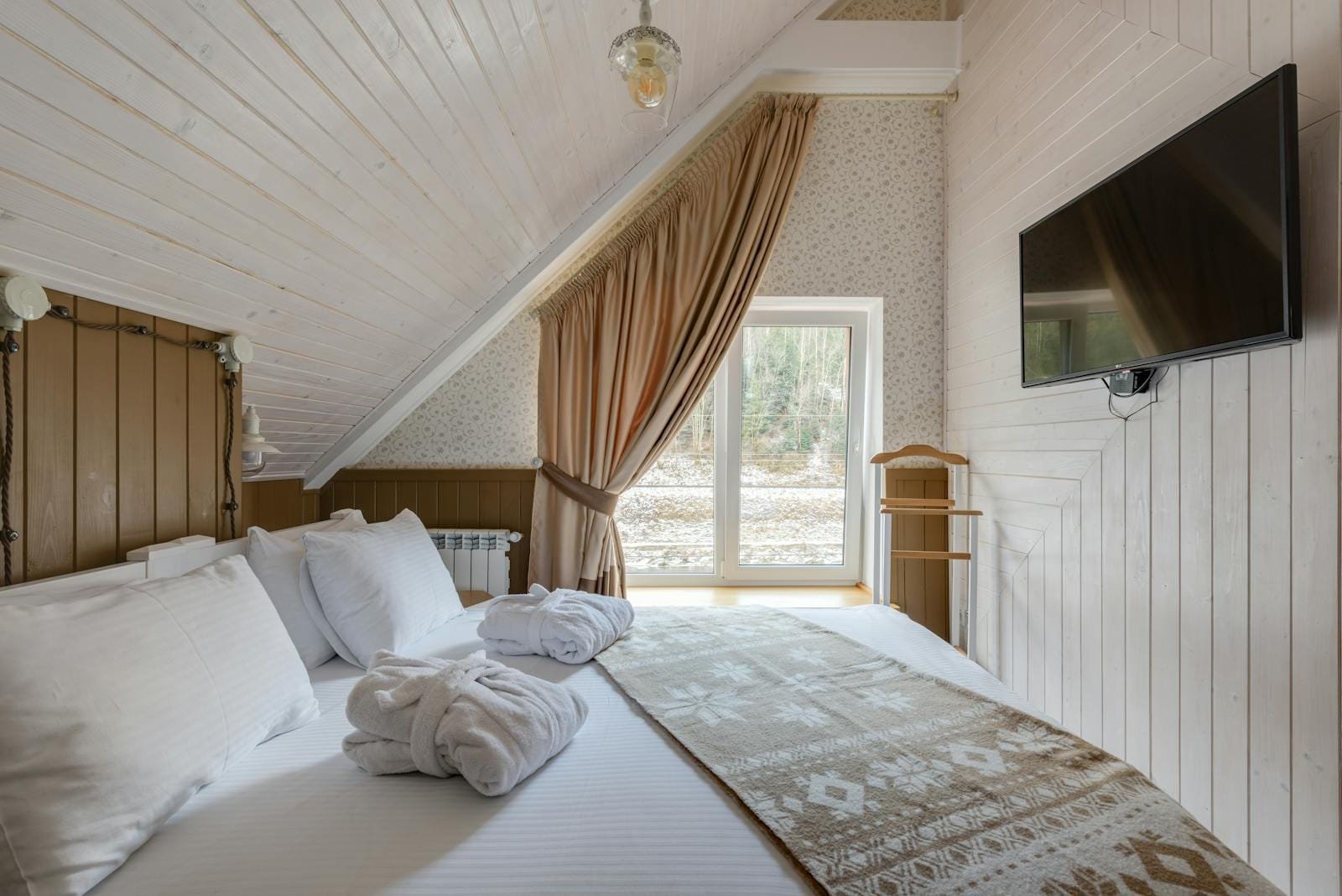 A comfortable attic bedroom features crisp linens, a TV, and ample natural light.