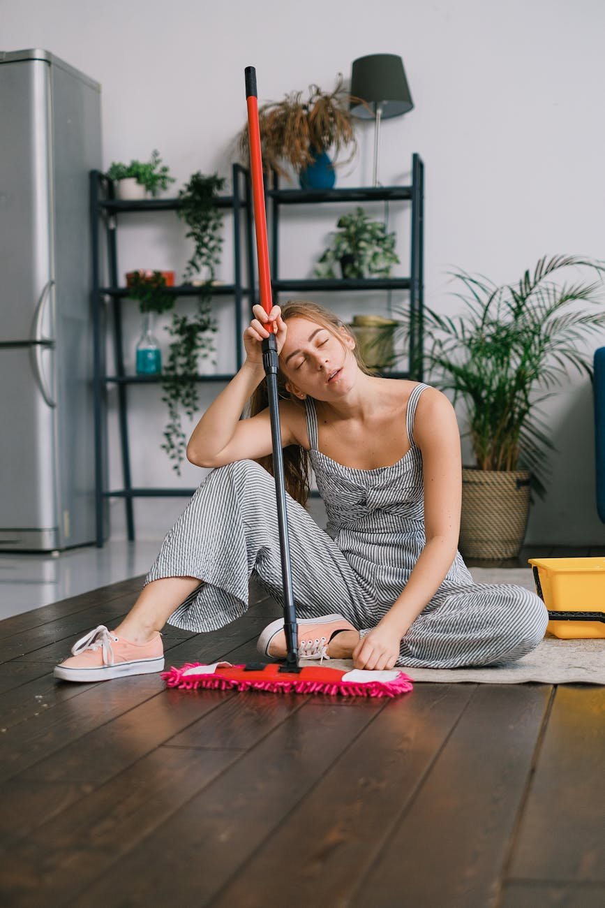 weary housewife with mop resting on rug at home