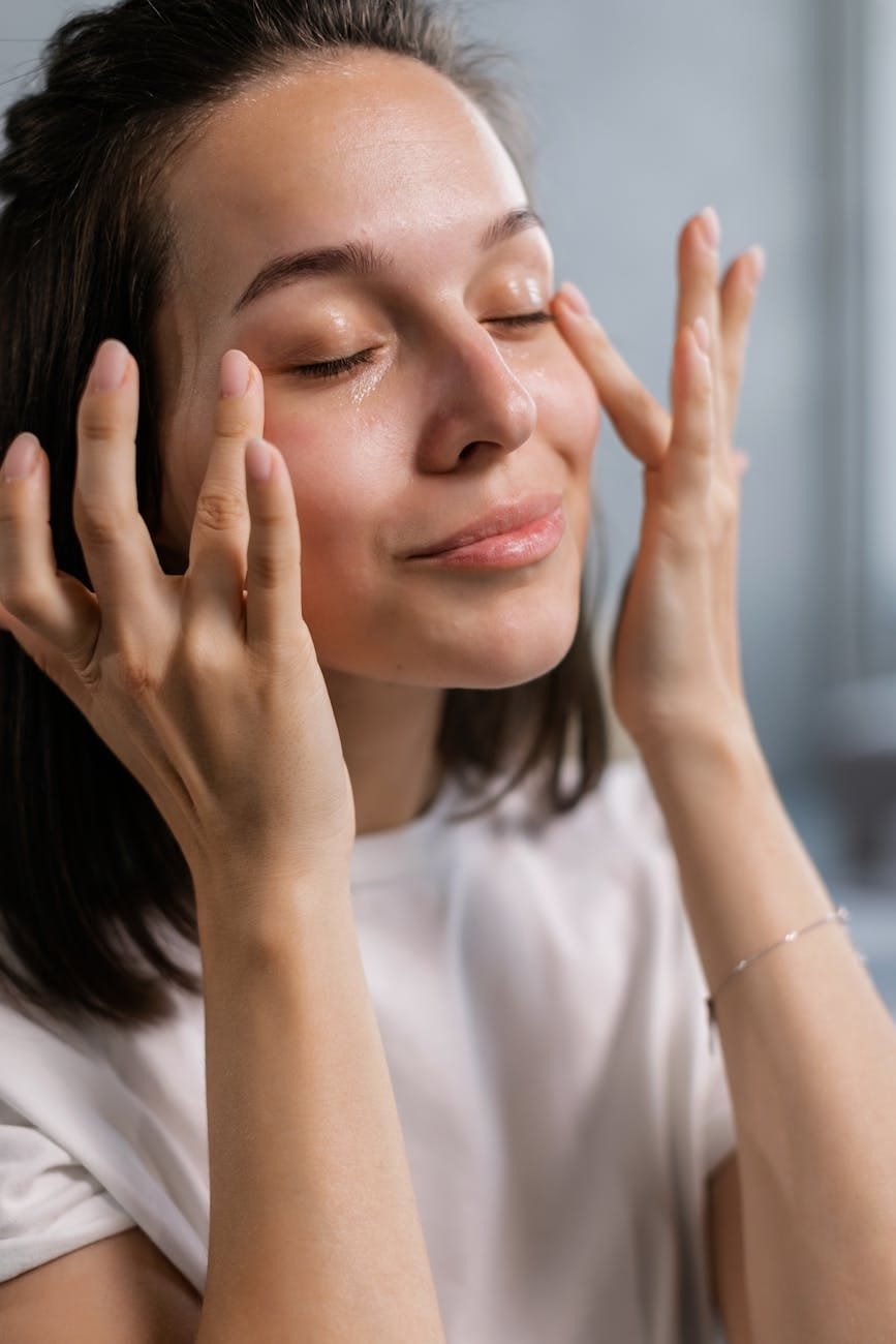 a woman in white shirt patting the sides of her eyes